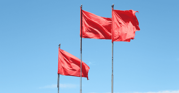 Life insurance red flags indicating potential scams or dishonest tactics by insurance agents, represented by three red flags waving in the wind.